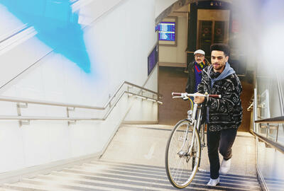 Ung mand med cykel på vej op ad trapper ved togstation