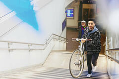 Ung mand med cykel på vej op ad trapper ved togstation