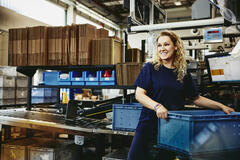 Smiling woman standing next to conveyer belt holding a crate