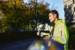Smiling male looking away wearing yellow jacket and walkie-talkie signing where to go
