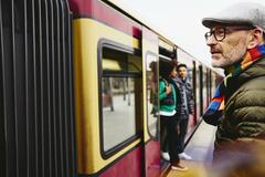 Man standing next to a train. Two people getting out of a train in the background.