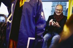 Man sitting in a bus, smiling, looking down at his phone.