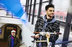 Man carrying a bike up the stairs in a train station. Other man walking up the stairs in the background.