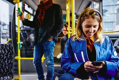 Smilende kvinde i bus, som ser på sin telefon