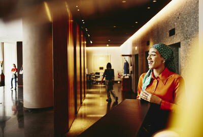 Smiling woman receptionist standing next to hotel reception desk.