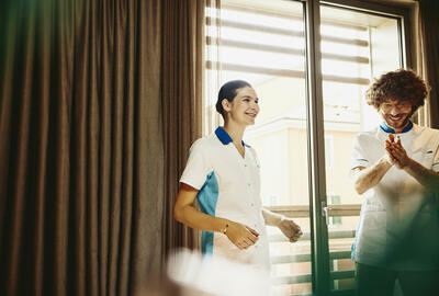 Two colleagues chatting, working housekeeping in a hotel room.