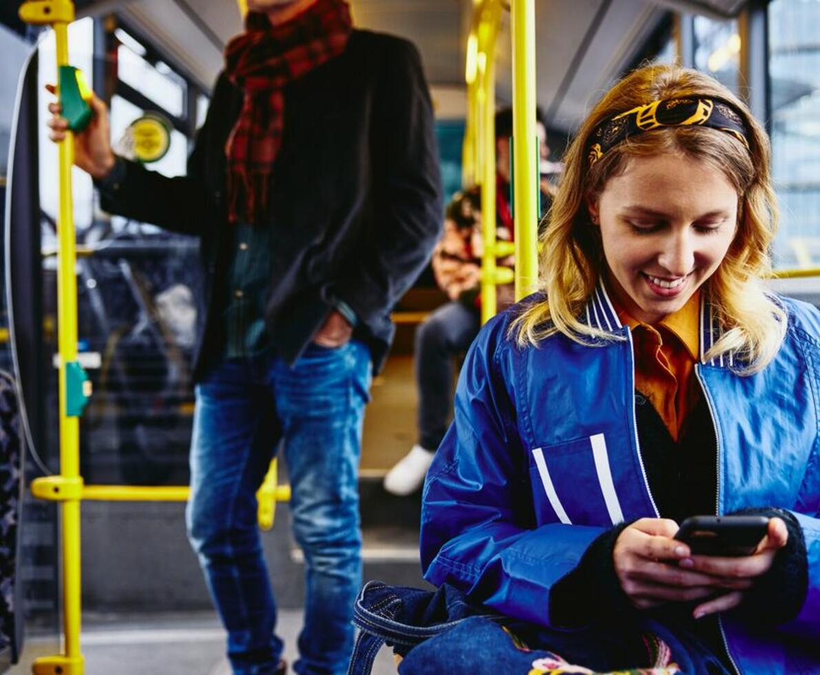 Smilende kvinde i bus, som ser på sin telefon