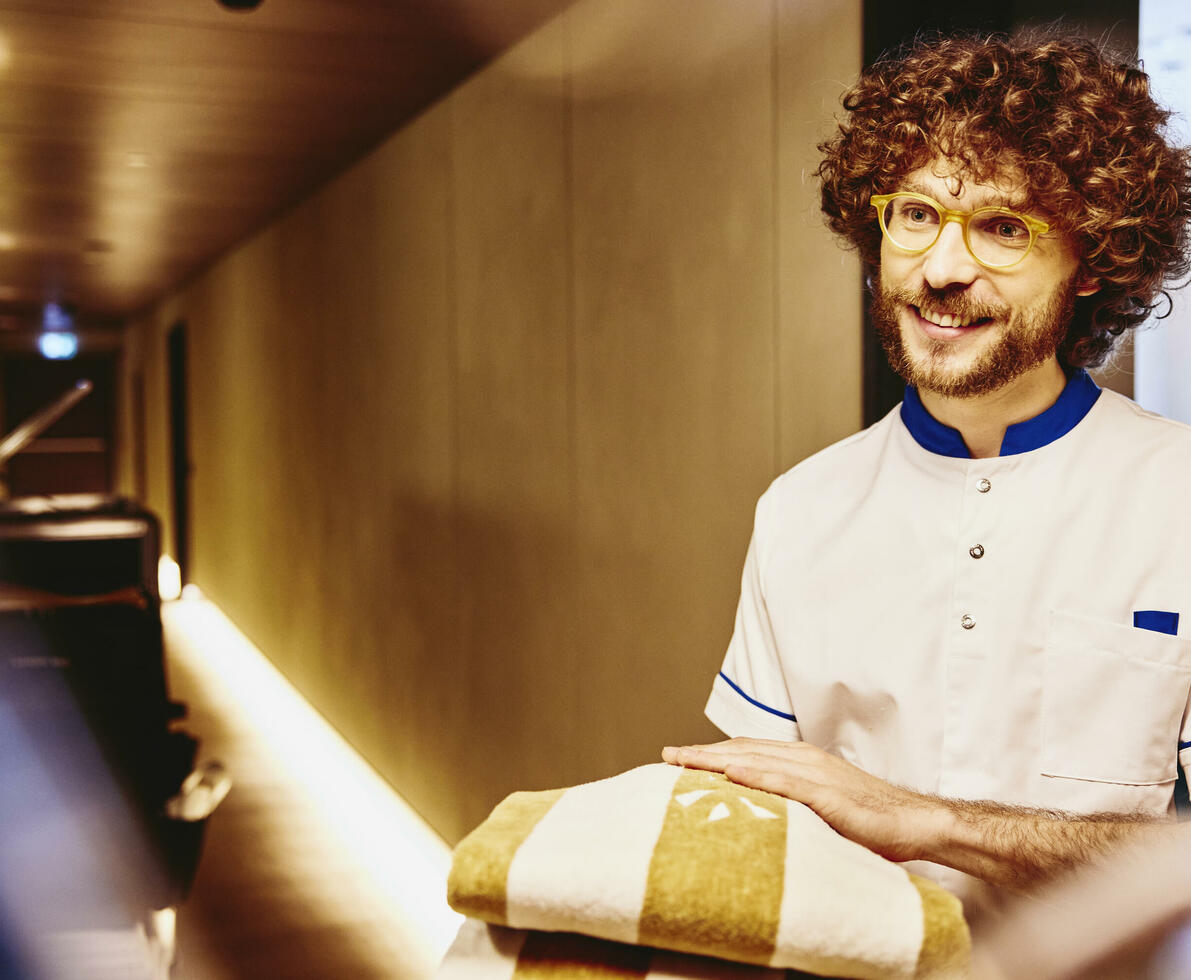 Man in uniform holding towels in a hallway of a hotel.